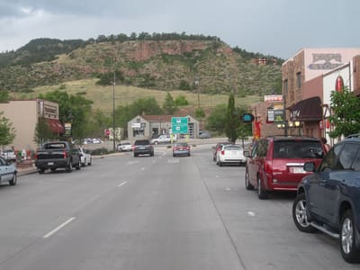 Main Street in Lyons looking west, with parked cars, the stone drug-store building on the right and the red sandstone hogback rising behind the town