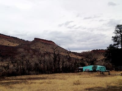 A meadow at dusk with the sandstone hogback and a turquoise cabin below it