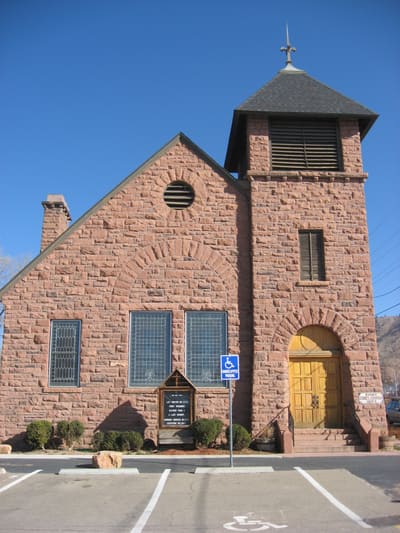 The rusticated sandstone front and bell tower of the Old Stone Church, with its arched yellow door
