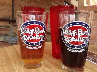 Two Oskar Blues Brewery pint glasses of beer on a bar