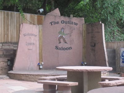 Three slabs of red Lyons sandstone carved with the words Welcome to Lyons, standing in a stone patio under cottonwoods