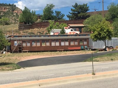 A vintage passenger rail car parked beside the road in Lyons, with the hogback behind